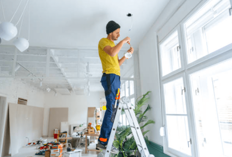 Muž stojaci na rebríku opravuje žiarovku